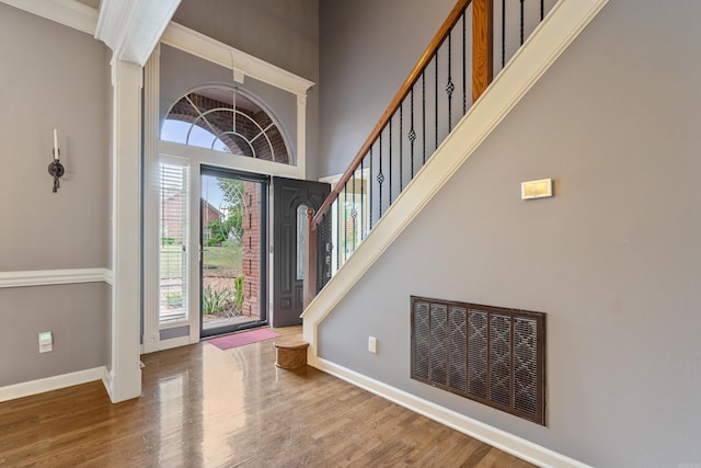 entrance foyer with a towering ceiling, baseboards, wood finished floors, and visible vents