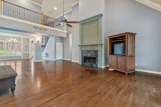unfurnished living room with a high ceiling, a premium fireplace, ceiling fan with notable chandelier, wood finished floors, and ornamental molding