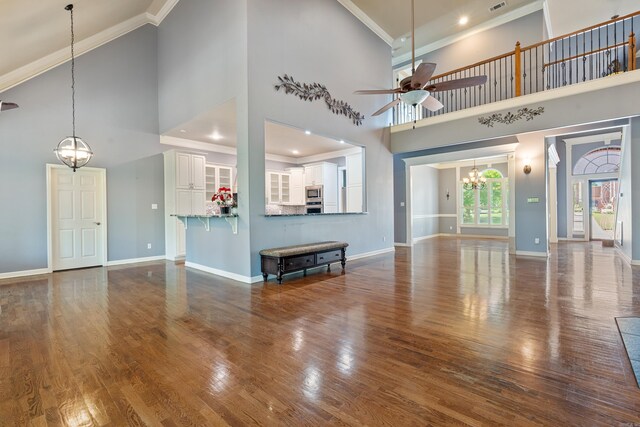 unfurnished living room with high vaulted ceiling, ornamental molding, baseboards, and ceiling fan with notable chandelier