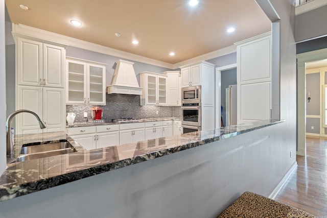 kitchen featuring crown molding, tasteful backsplash, custom range hood, a sink, and stainless steel appliances