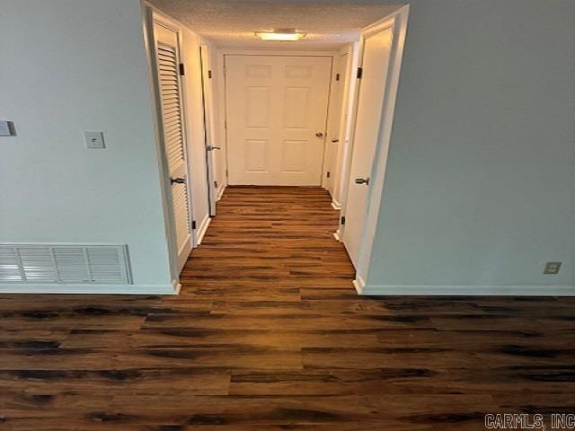 hall featuring baseboards, visible vents, and dark wood-style floors