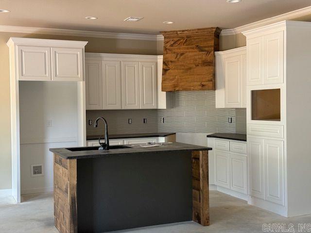 kitchen with crown molding, dark countertops, and a kitchen island with sink
