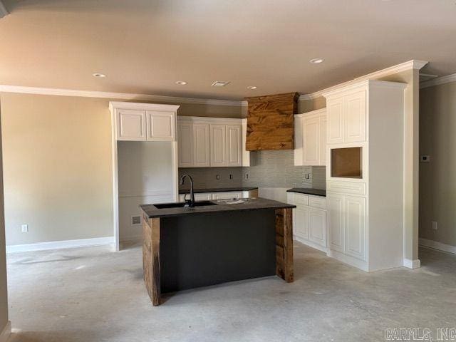 kitchen featuring dark countertops, tasteful backsplash, a center island with sink, a sink, and ornamental molding