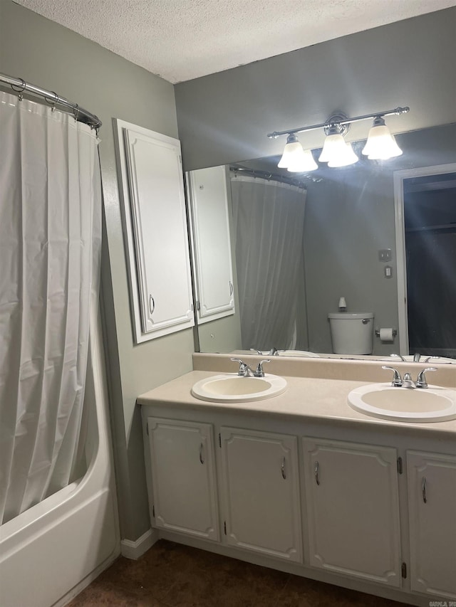 bathroom with toilet, double vanity, a textured ceiling, and a sink