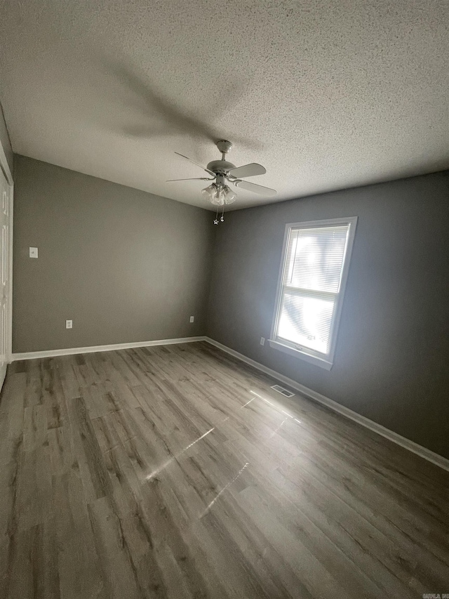 spare room featuring a textured ceiling, ceiling fan, wood finished floors, and visible vents