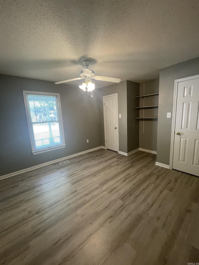 unfurnished bedroom with baseboards, a textured ceiling, wood finished floors, and visible vents