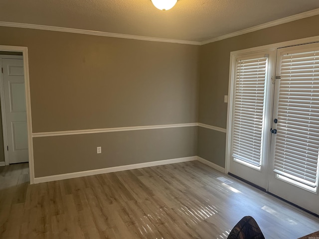 empty room with a textured ceiling, visible vents, wood finished floors, baseboards, and ornamental molding