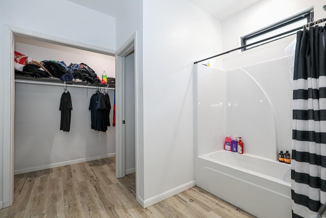 full bathroom with baseboards, a walk in closet, wood finished floors, and shower / bath combo