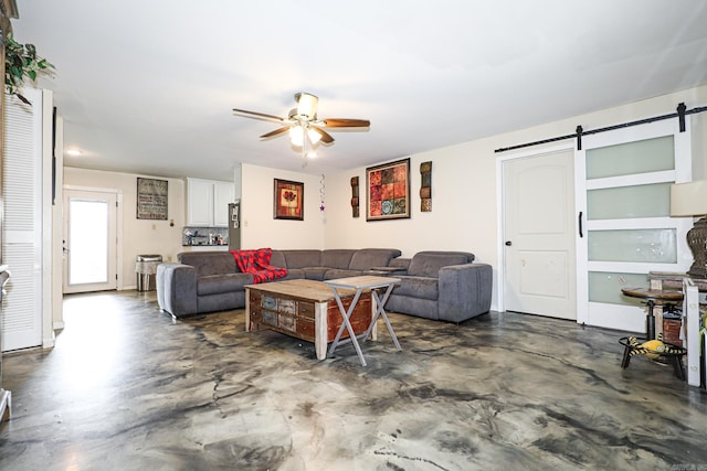 living area with a barn door, concrete floors, and a ceiling fan