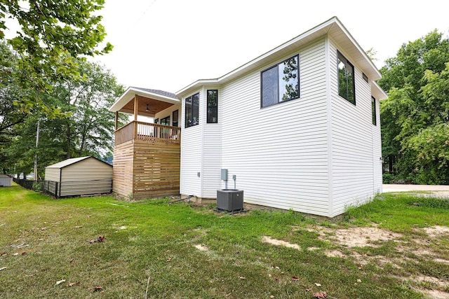 rear view of house featuring a storage shed, an outbuilding, cooling unit, a lawn, and a ceiling fan
