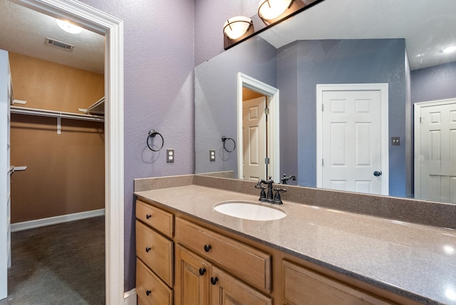 bathroom featuring a textured wall, visible vents, a walk in closet, and vanity
