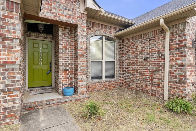 property entrance featuring brick siding and a shingled roof