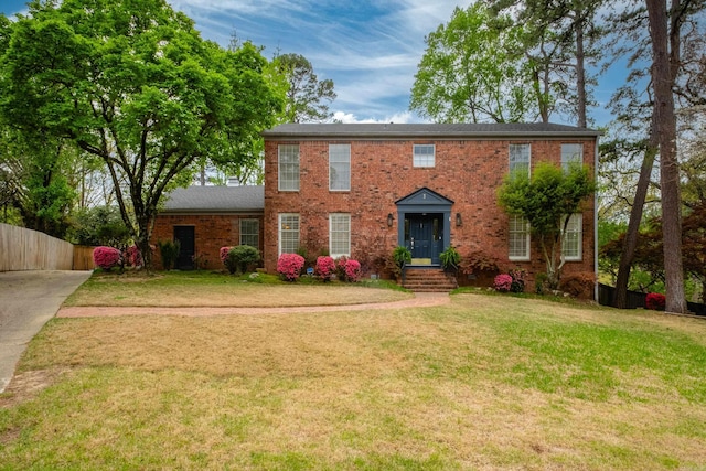 colonial inspired home featuring fence, a front lawn, and brick siding