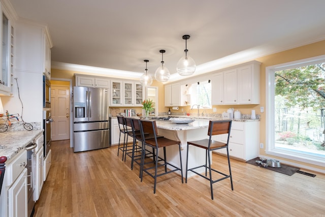 kitchen with light wood finished floors, appliances with stainless steel finishes, a breakfast bar area, and a healthy amount of sunlight
