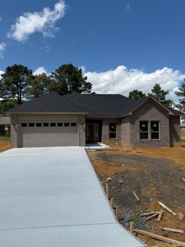 single story home with an attached garage, a shingled roof, brick siding, and concrete driveway