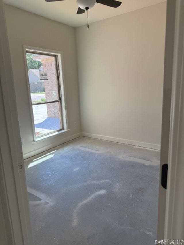 unfurnished room featuring baseboards, ceiling fan, concrete flooring, and a wealth of natural light