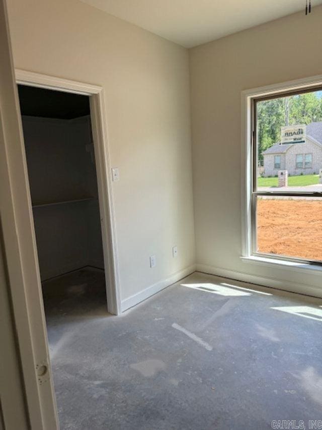 unfurnished bedroom featuring baseboards, unfinished concrete flooring, and a spacious closet