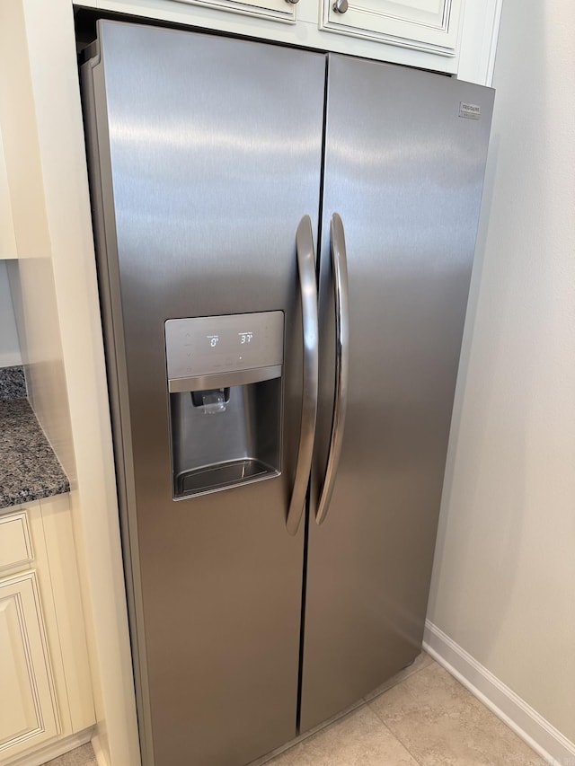 interior details featuring cream cabinets, stainless steel refrigerator with ice dispenser, baseboards, and dark stone countertops