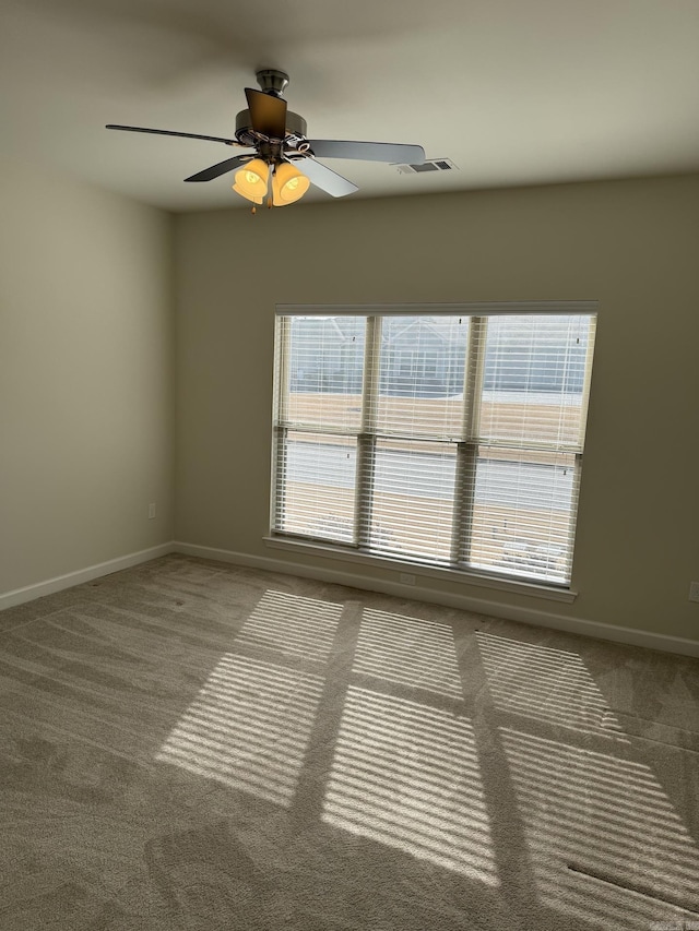 carpeted spare room with baseboards, a ceiling fan, and visible vents