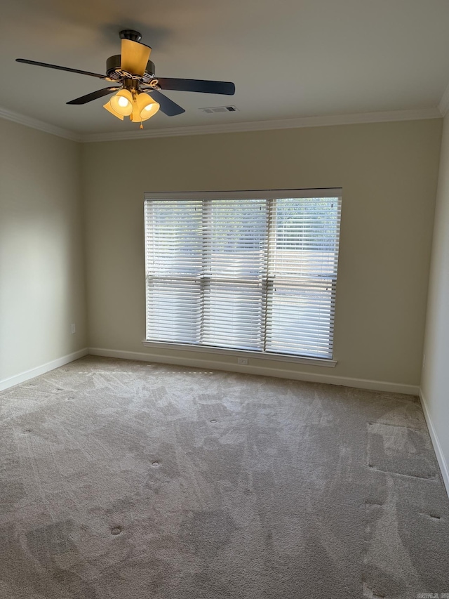 carpeted spare room featuring crown molding, baseboards, a ceiling fan, and visible vents