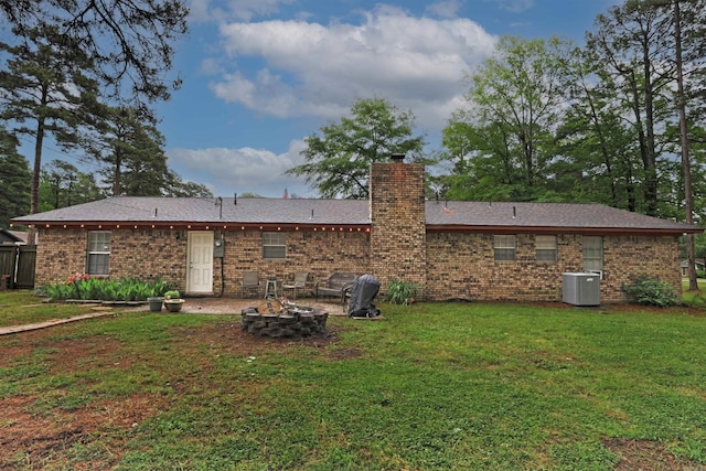 rear view of property with a fire pit, central AC, a chimney, brick siding, and a lawn