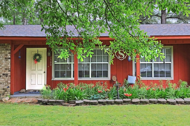 doorway to property featuring a shingled roof and a yard