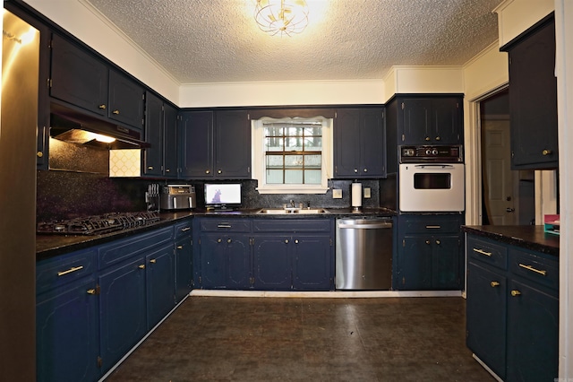 kitchen with dark countertops, a textured ceiling, under cabinet range hood, a sink, and stainless steel appliances