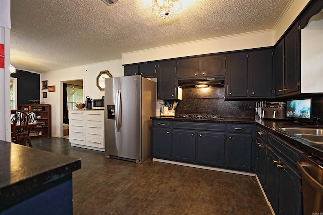 kitchen featuring decorative backsplash, dark countertops, a textured ceiling, under cabinet range hood, and appliances with stainless steel finishes
