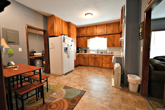 kitchen featuring white refrigerator with ice dispenser, light countertops, electric panel, brown cabinets, and a sink