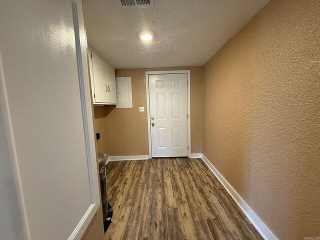 clothes washing area featuring a textured wall, baseboards, and dark wood-type flooring