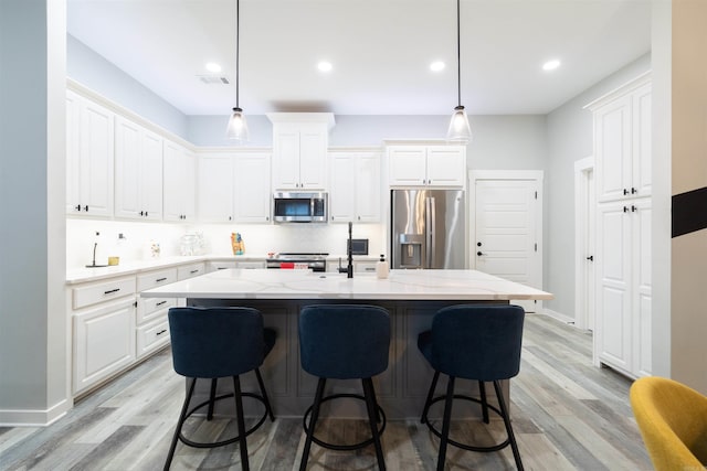 kitchen featuring appliances with stainless steel finishes, light wood-style floors, a breakfast bar area, visible vents, and a center island with sink