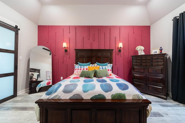 bedroom featuring baseboards, a barn door, light wood-style flooring, and lofted ceiling