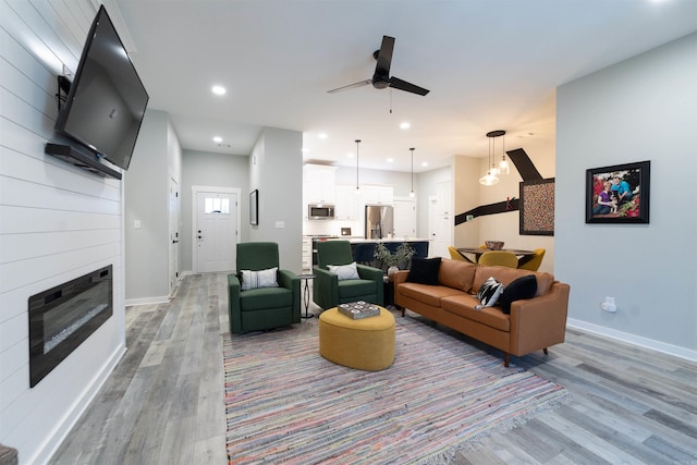 living area with a ceiling fan, baseboards, light wood finished floors, and a fireplace