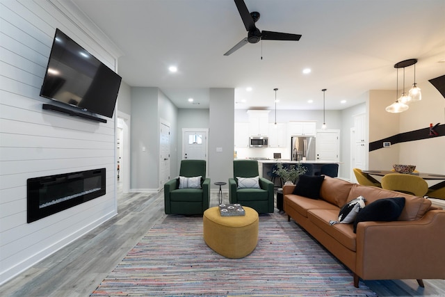 living area featuring ceiling fan, a fireplace, recessed lighting, baseboards, and wood finished floors