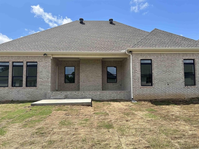 back of property with a lawn, a patio, a shingled roof, and brick siding