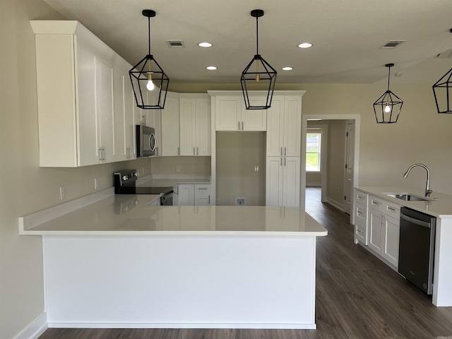 kitchen featuring dark wood-style flooring, a peninsula, light countertops, a sink, and appliances with stainless steel finishes