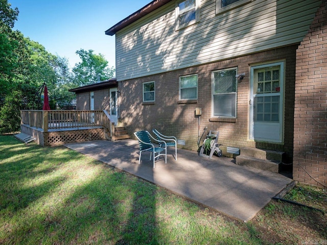 back of house featuring brick siding, a deck, entry steps, a patio area, and a lawn