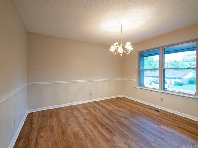 empty room with visible vents, baseboards, wood finished floors, and a notable chandelier