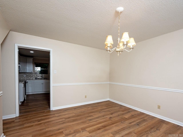 unfurnished dining area with baseboards, a textured ceiling, wood finished floors, and a notable chandelier