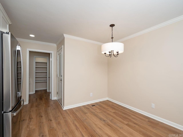 unfurnished dining area featuring crown molding, baseboards, light wood-style floors, and an inviting chandelier