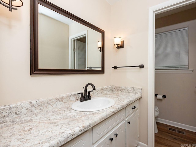 bathroom featuring visible vents, wood finished floors, vanity, baseboards, and toilet