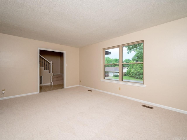 empty room featuring light colored carpet, baseboards, visible vents, and stairway