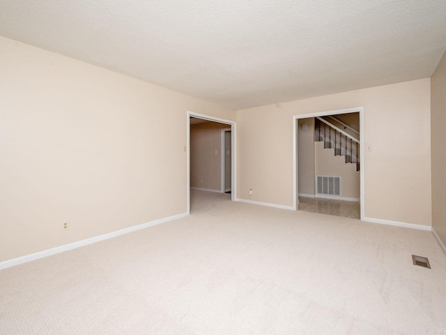 empty room featuring visible vents, baseboards, stairway, and light colored carpet