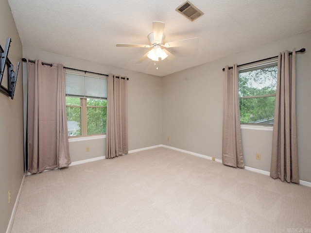 spare room with a ceiling fan, light colored carpet, visible vents, and a healthy amount of sunlight