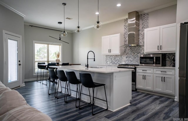 kitchen with ornamental molding, wall chimney range hood, a sink, appliances with stainless steel finishes, and backsplash