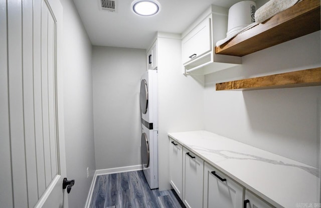 mudroom featuring dark wood-style flooring, baseboards, visible vents, and stacked washer and clothes dryer