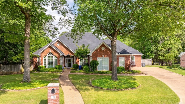 traditional-style home with fence, roof with shingles, brick siding, a front yard, and driveway
