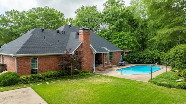 back of property with a patio, an outdoor pool, a chimney, brick siding, and a yard