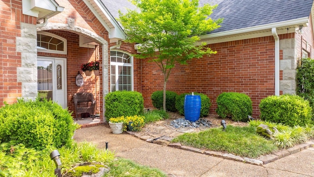 property entrance featuring a shingled roof and brick siding