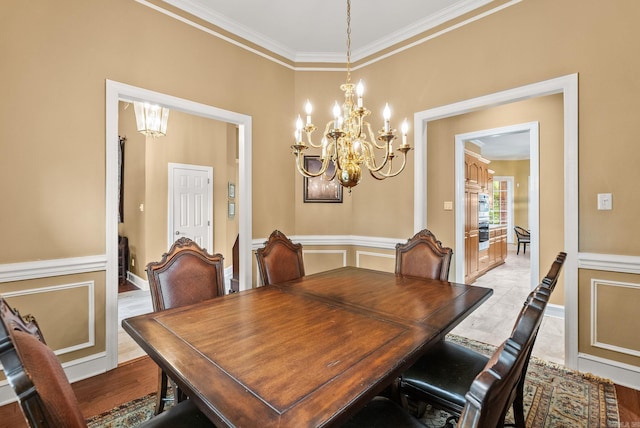 dining space with crown molding, a chandelier, and a wainscoted wall